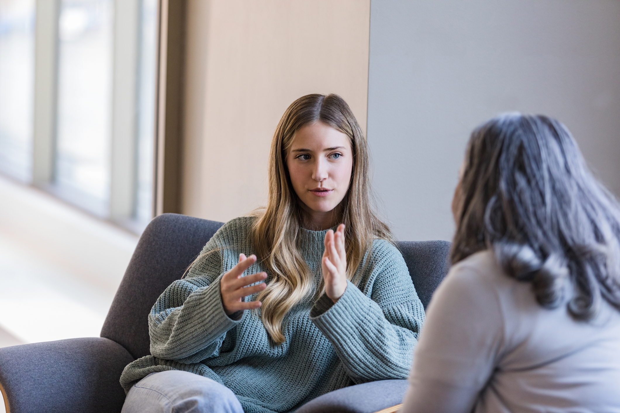 The young adult university student gestures and shares her struggles when she meets with an unrecognizable therapist in her office on campus.